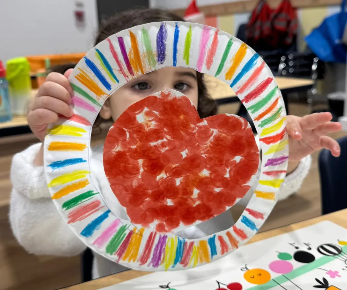 A child at GrowVille holds up a colourful paper-plate heart craft